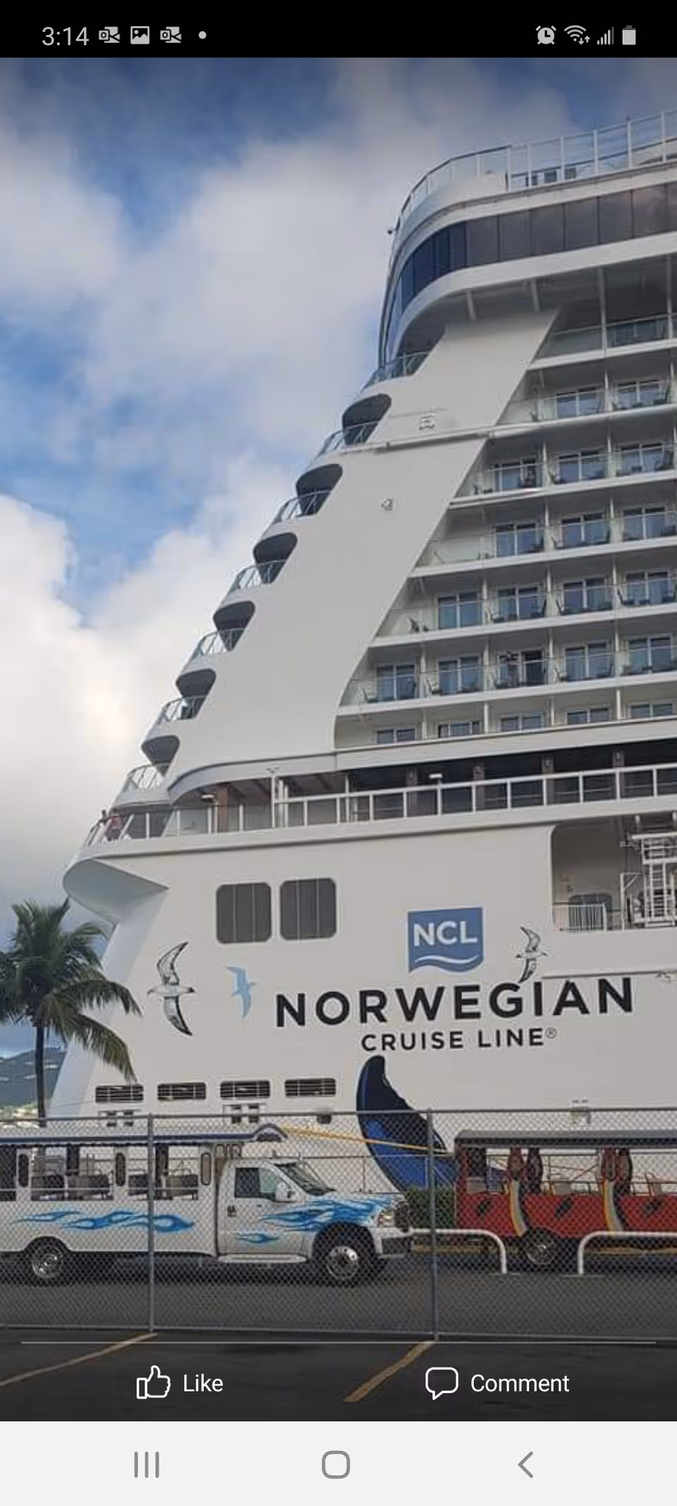 Large white Norwegian Cruise Line ship with a fenced pier area and parked vans.