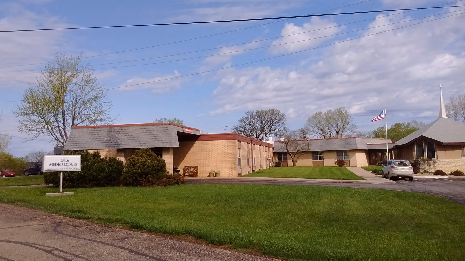 Exterior view of a single-story Medicalodges facility with a sign and green lawn