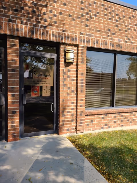 Brick exterior of a building with a glass door and large window displaying Nightingale logo.