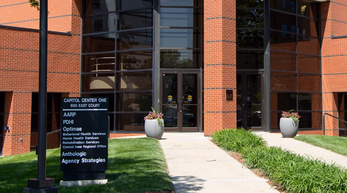 Brick building exterior with glass doors, walkway, and potted plants at Optimae entrance.