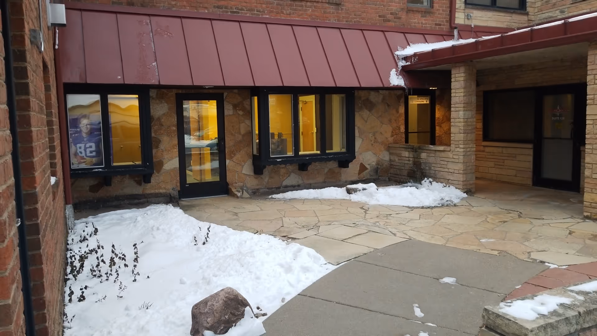 Snowy outdoor entry to a senior living facility with stone walls and red awning.