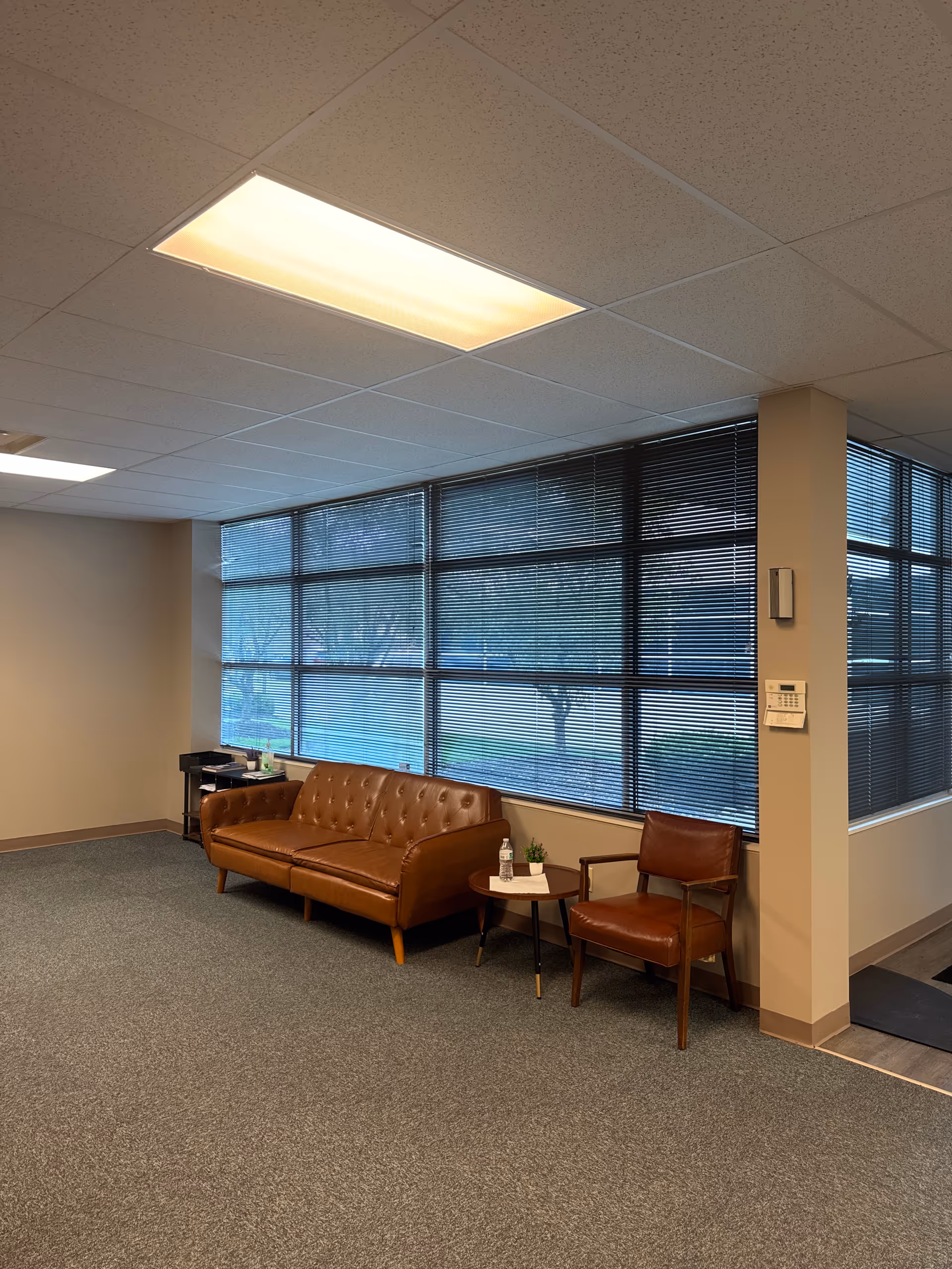 Lobby-style living room with brown leather sofa, chair, side table, and large windows.