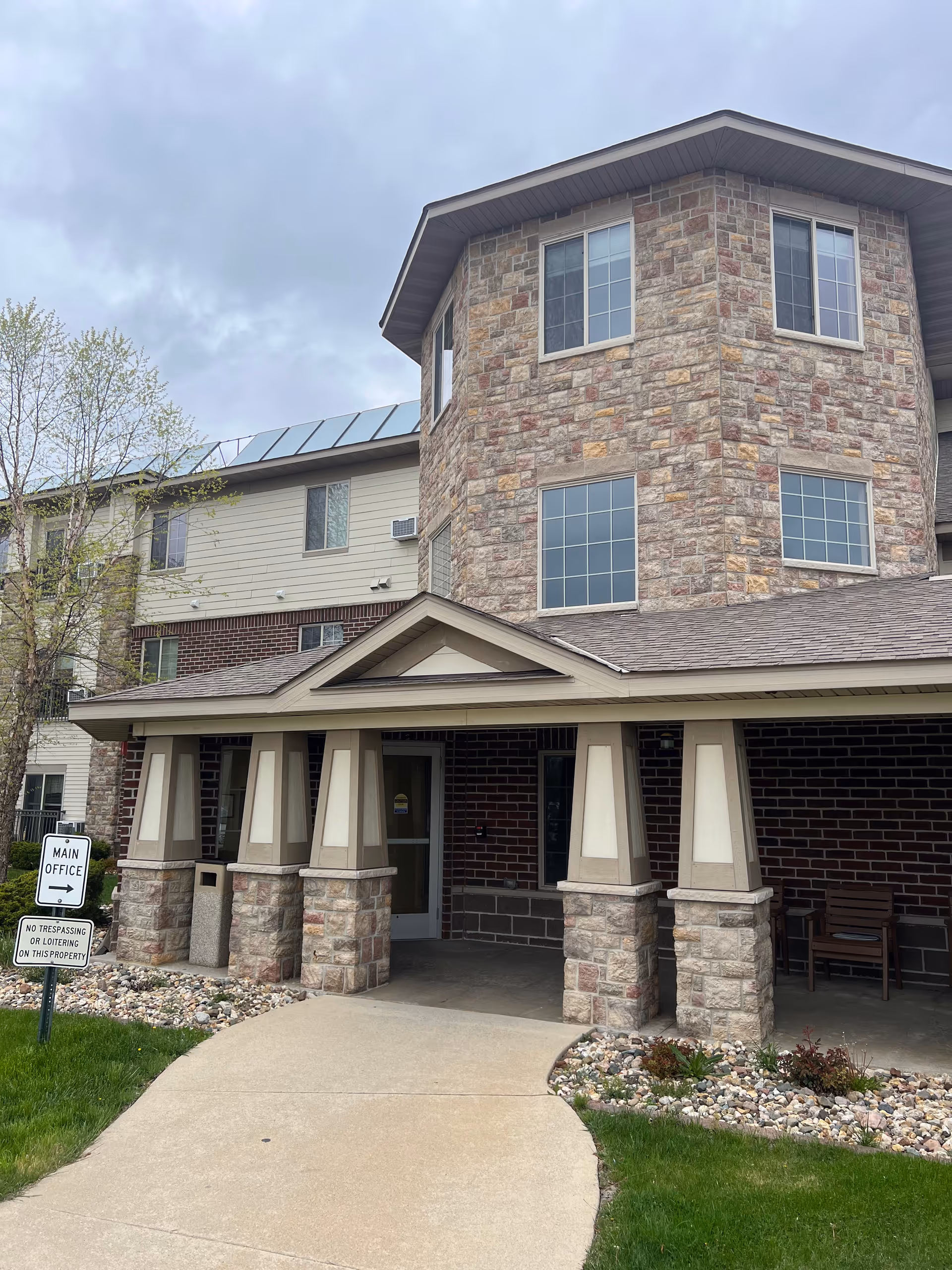 Stone-facade senior living entrance with walkway, sign, and landscaped front.