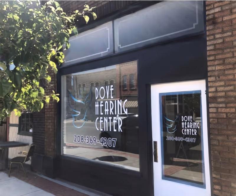 Exterior of Dove Hearing Center storefront with large window sign and white door.