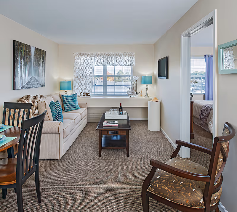 Cozy living room with beige sofa, coffee table, windows, and doorway to a bedroom.