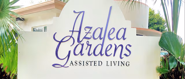 Exterior view of Azalea Gardens Assisted Living sign with tropical plants surrounding.
