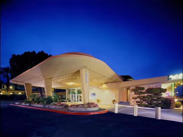 Curved illuminated entrance canopy at a senior living facility with landscaped planters at dusk.