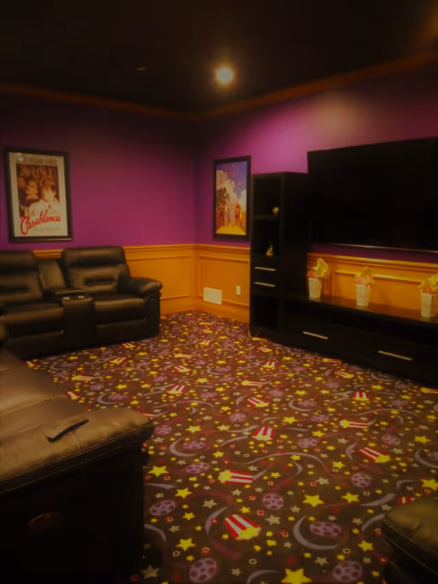 Purple-walled lounge with black leather recliners, a TV, and a colorful patterned carpet.