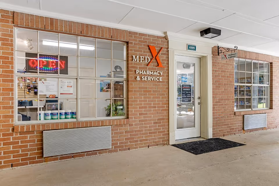 Brick building exterior with a pharmacy storefront and open sign in windows.