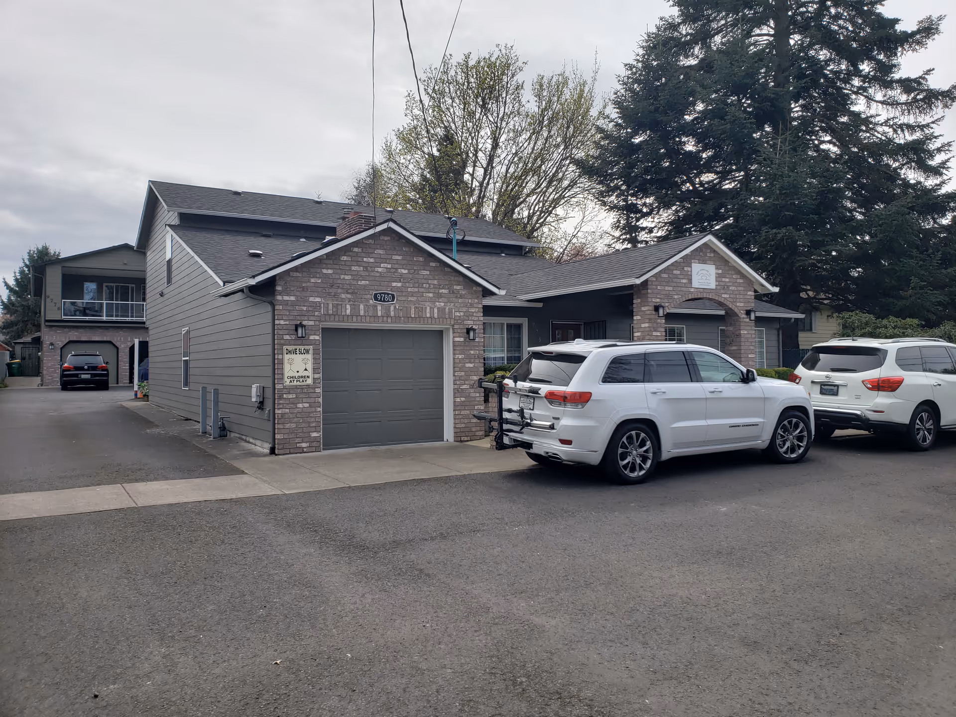 Exterior view of a brick senior care home with parked SUVs and a driveway.