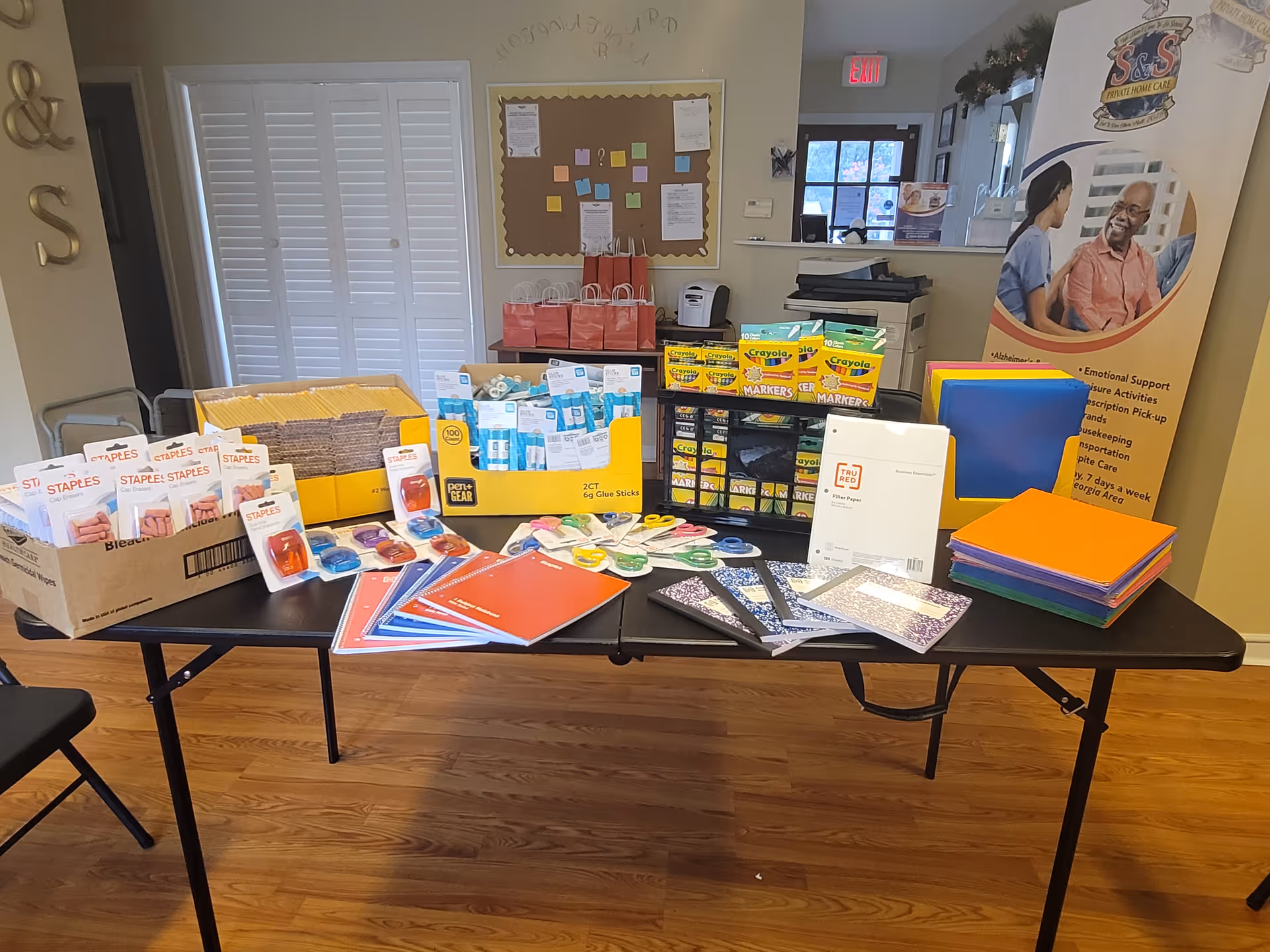 Assorted school and office supplies arranged on a table in a bright room.