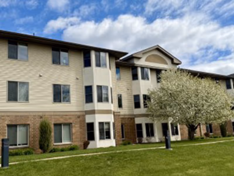 Exterior view of Heritage Place of Roseville, a multi-story senior living building with trees.