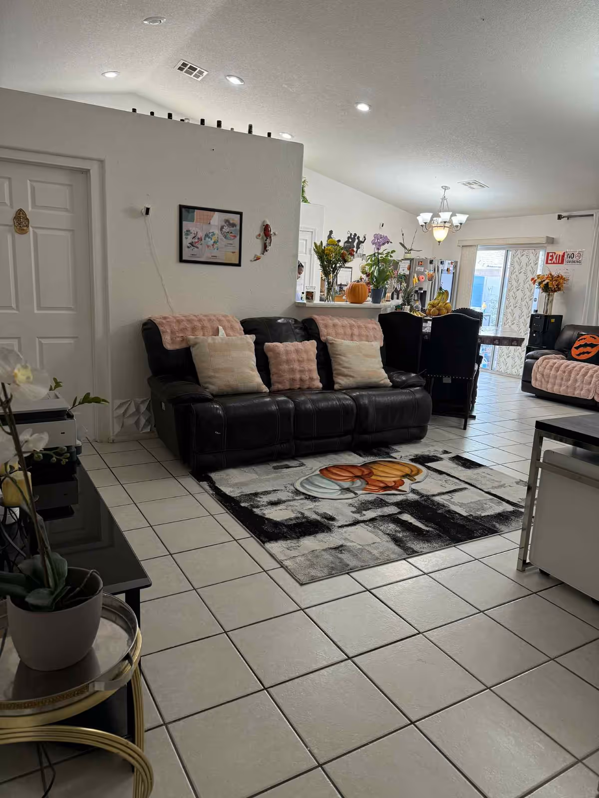 Cozy living room with black leather sectional, pink pillows, and a visible kitchen/dining area.
