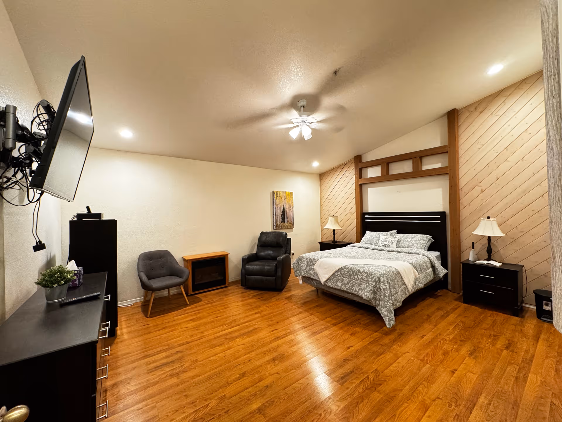 A spacious bedroom with a large bed, seating area, and mounted TV in a modern suite.