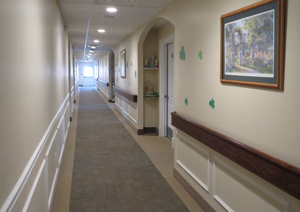Long, well-lit hallway in a senior living facility with artwork and shamrock decorations.