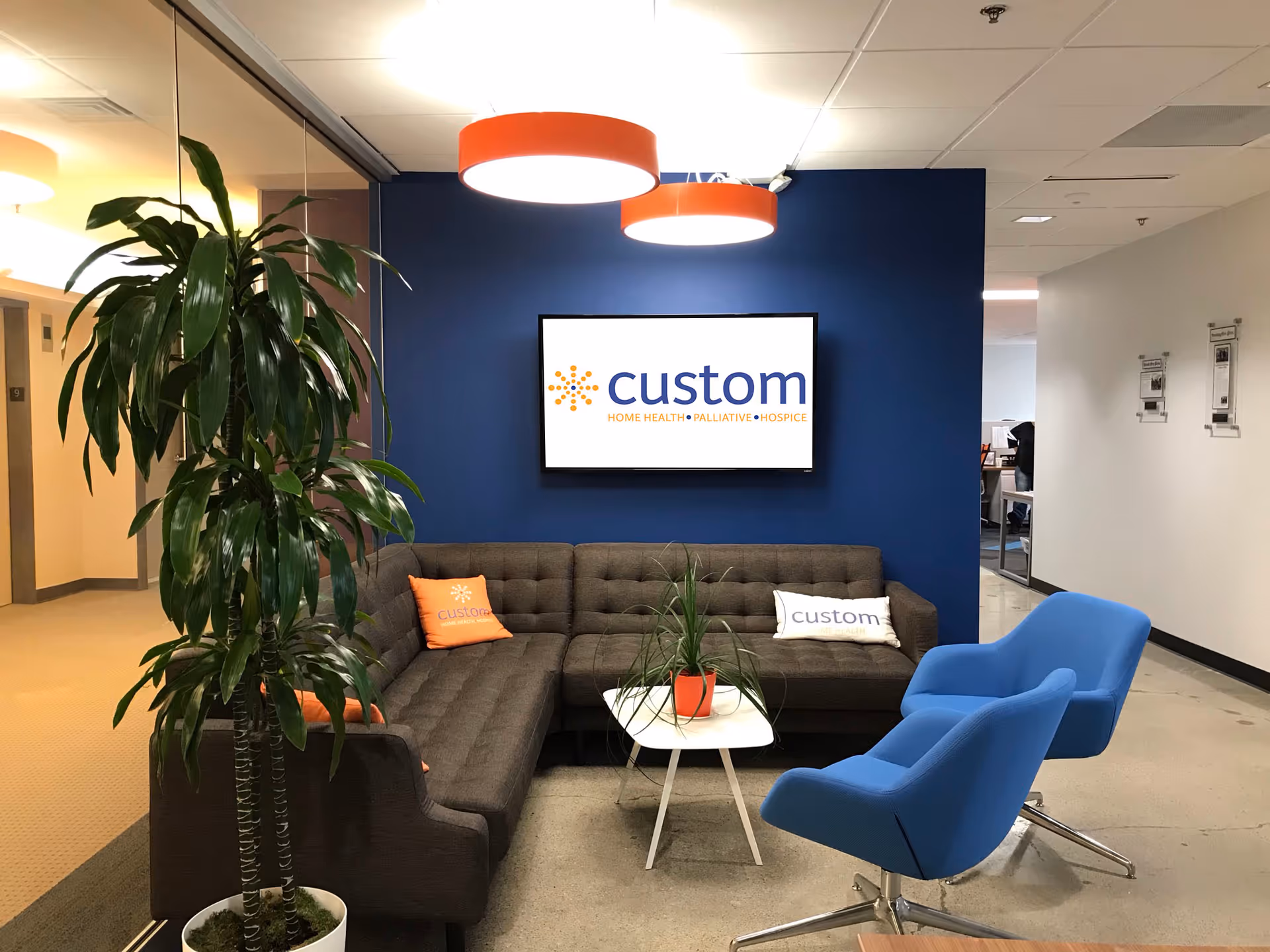 Lounge area with blue wall, orange pendant lights, sofa, blue chairs, and a Custom sign.