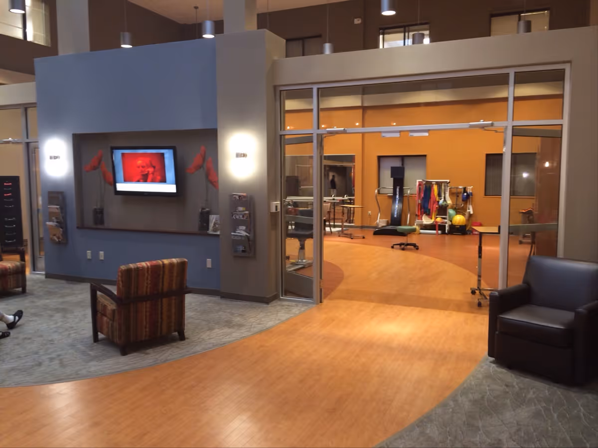 Lobby seating area with wall TV and glass doors to a fitness room.