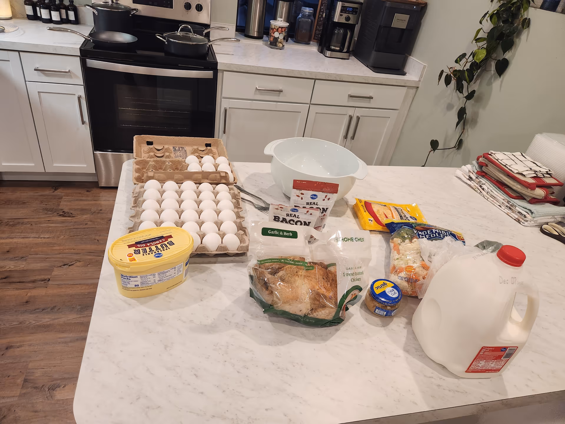 Kitchen island with eggs, milk jug, groceries, bread, and appliances on white cabinetry.