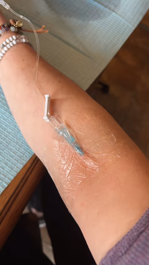 Forearm with IV catheter taped and tubing, bracelets visible, in a clinical interior