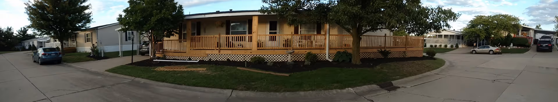 Panoramic exterior of Princeton Crossing senior living facility with a wooden front porch and trees.
