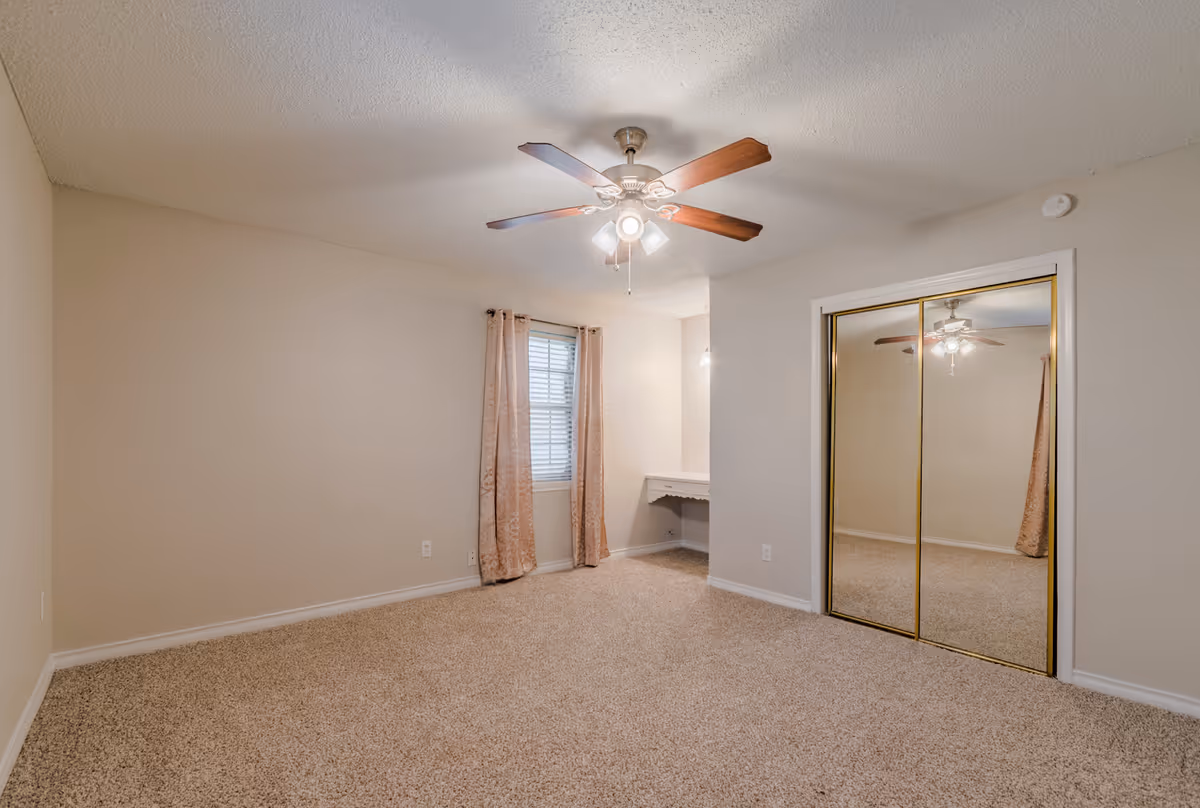 Empty beige Heritage Hill Home bedroom with carpet, ceiling fan, window, curtains, and mirrored closet.