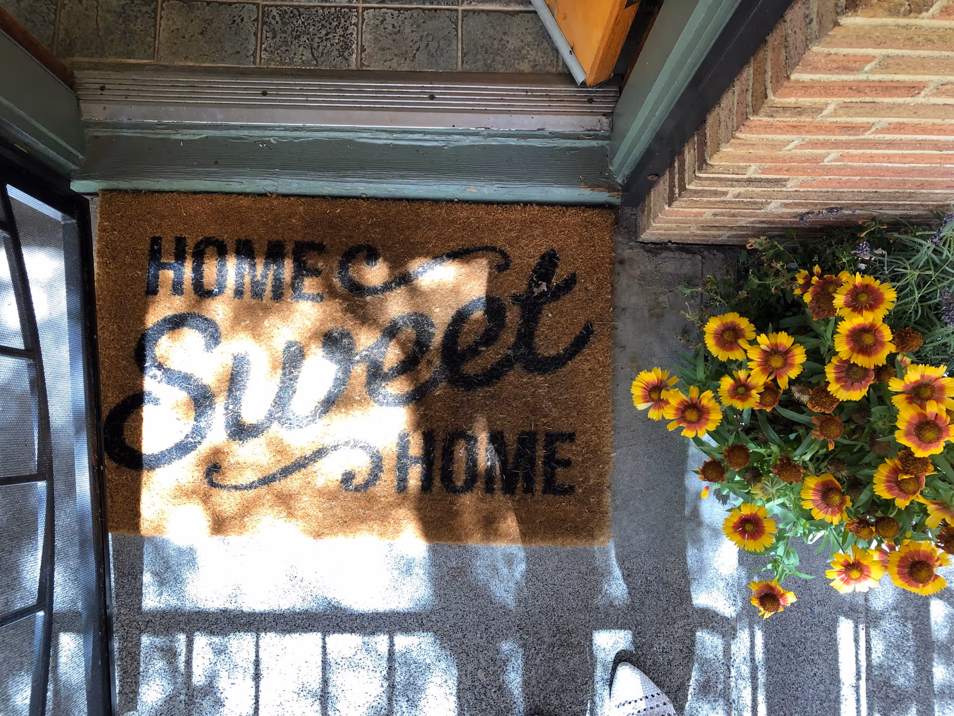 Front entrance with Home Sweet Home doormat and a yellow flower planter beside the door.