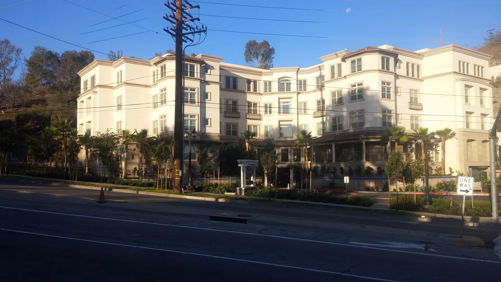 A large cream-colored senior living building with palm trees along a street.