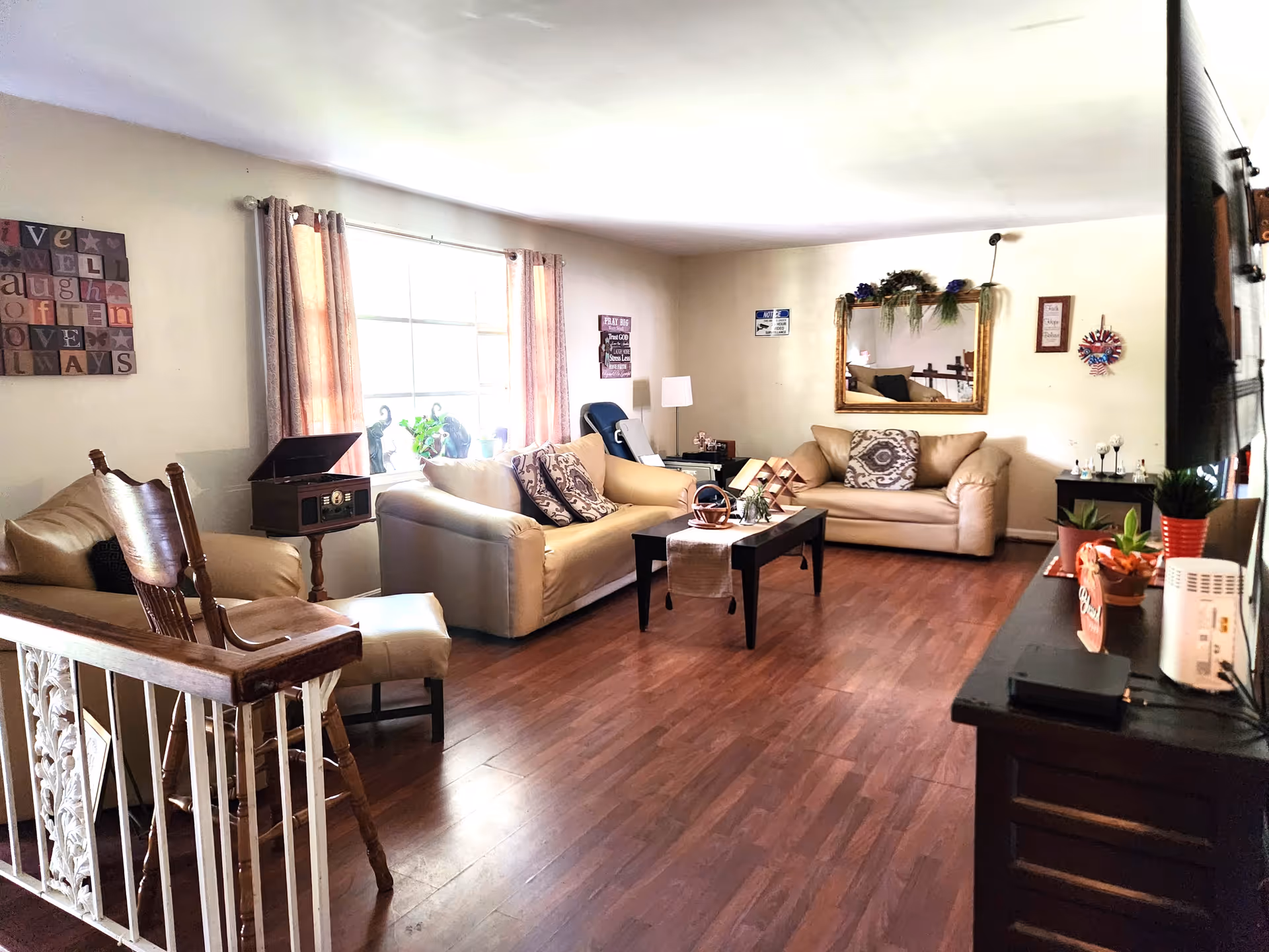 Bright living room with beige sofas, coffee table, and decorative wall mirror in a senior facility.
