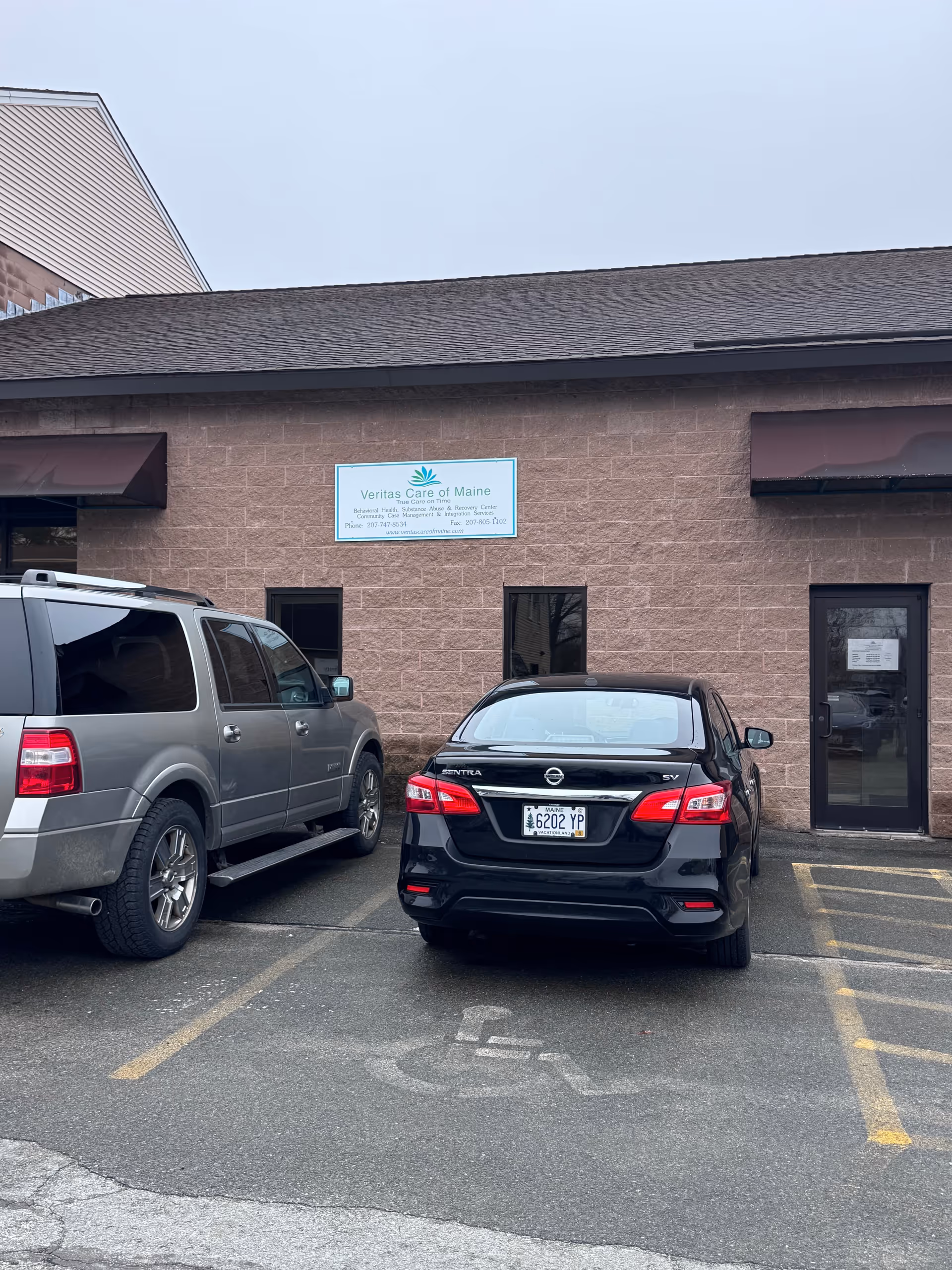 Brick building exterior with Veritas Care of Maine sign and two parked cars.