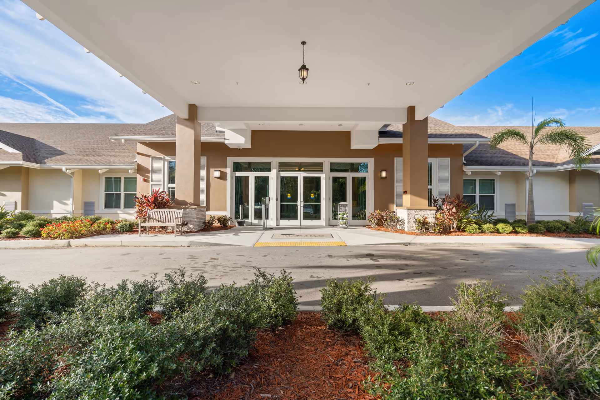 Entrance of a senior living facility with glass doors and landscaped walkway.