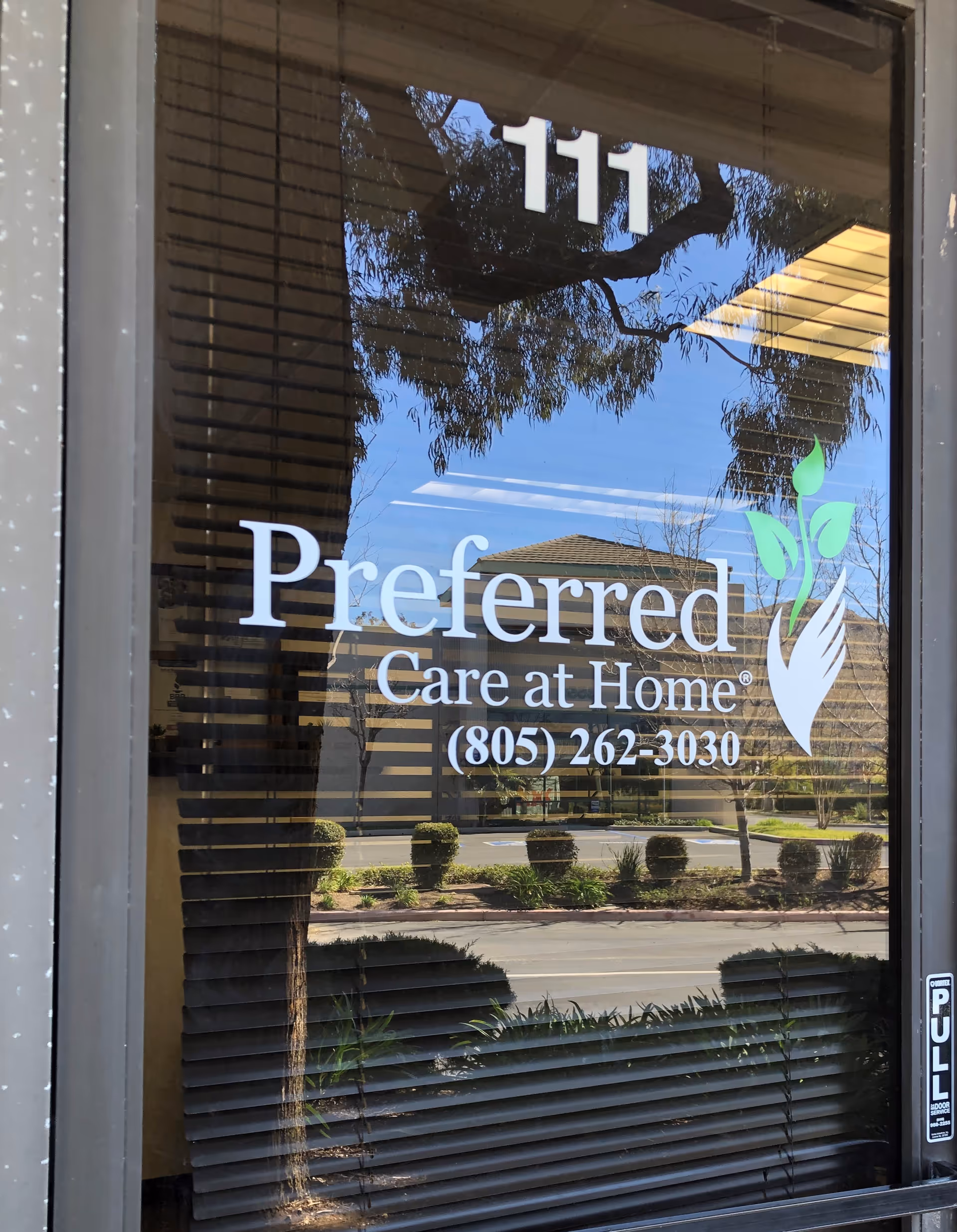 Glass door shows Preferred Care at Home logo with reflections of trees.