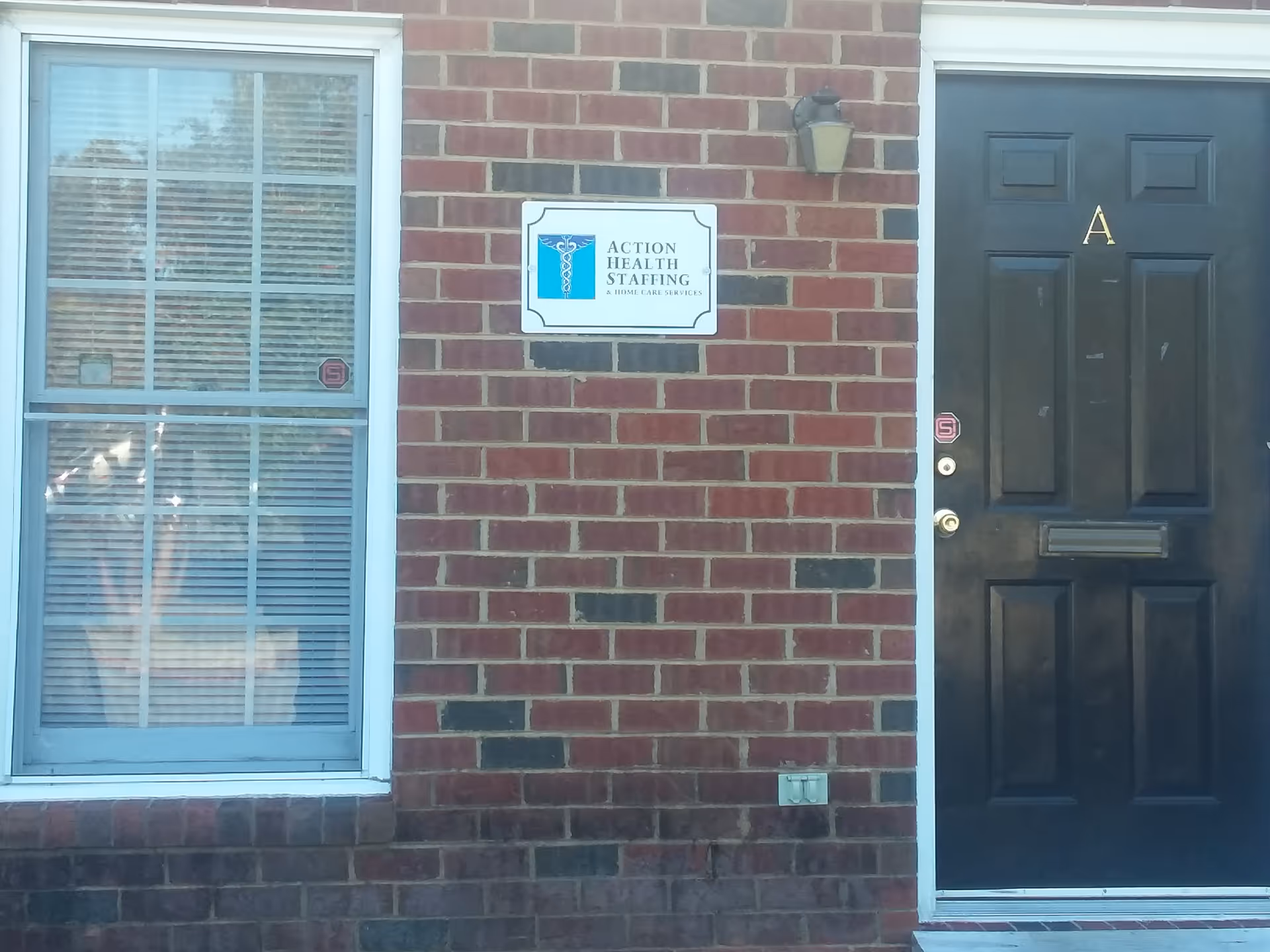 Brick exterior with a window, dark door, and Action Health Staffing sign.