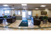 Lobby lounge with brown leather chairs, plants, lamps, and a back doorway.