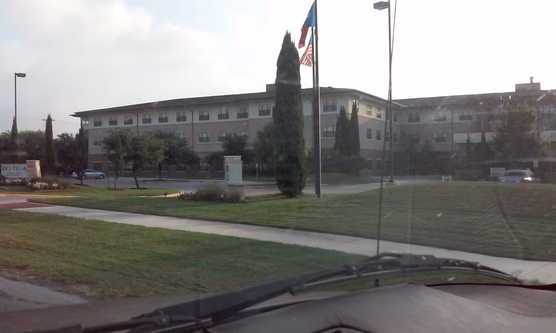 Exterior view of Rio Terra Senior Living building with flagpoles and well-kept lawn.