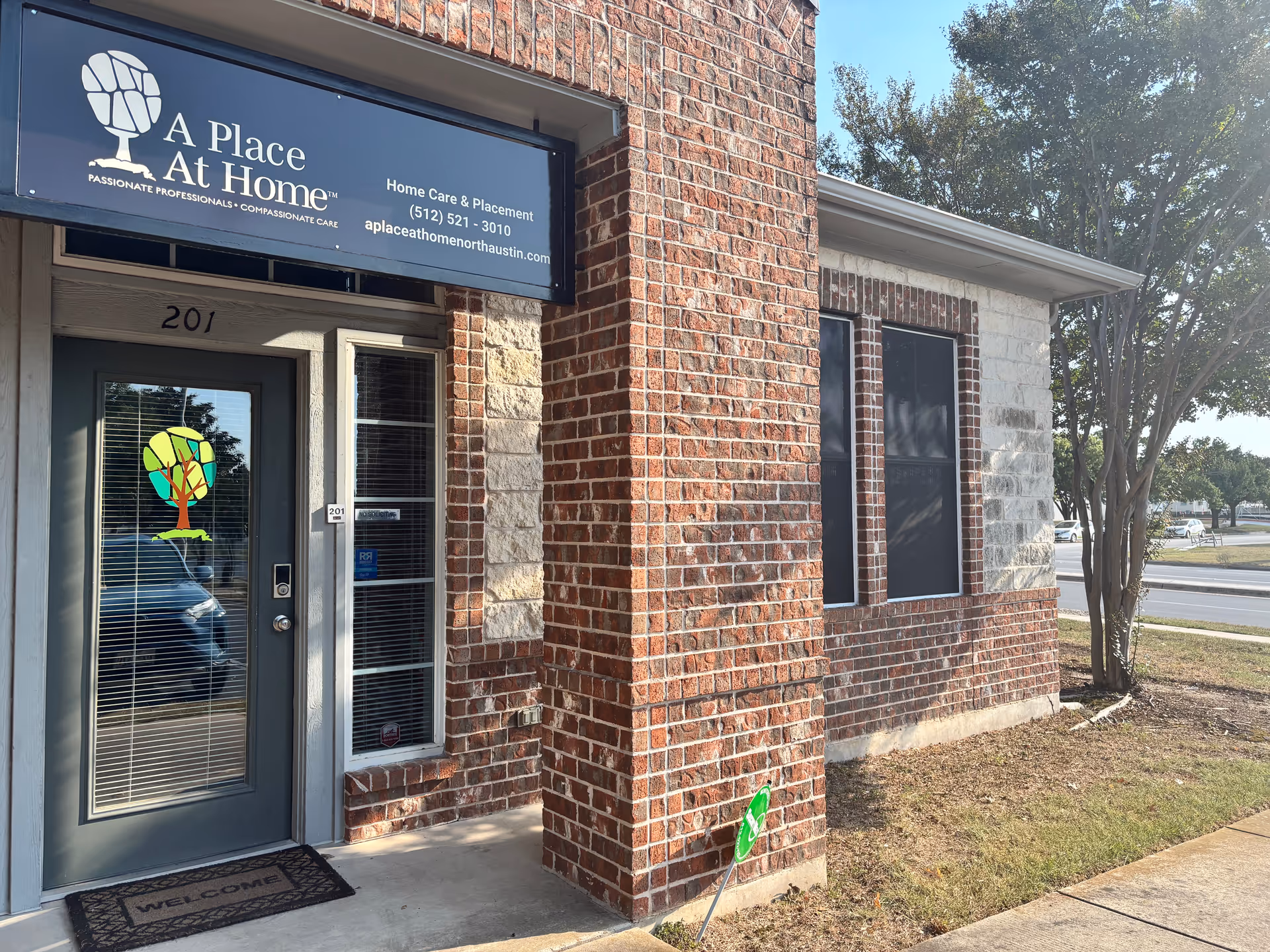 Brick building entrance with A Place At Home North Austin sign and glass door.