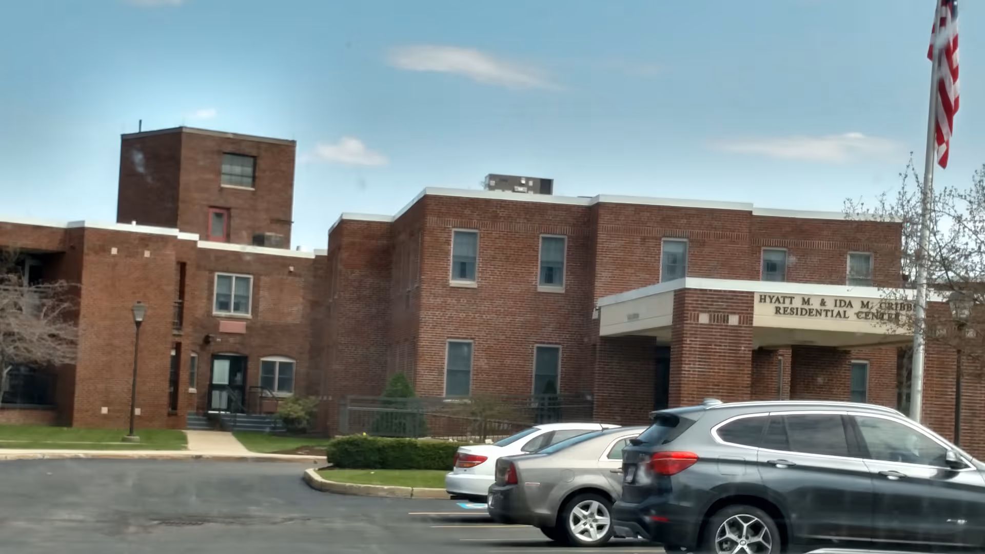 Wesbury United Methodist senior living facility exterior with entrance, cars, and flag.
