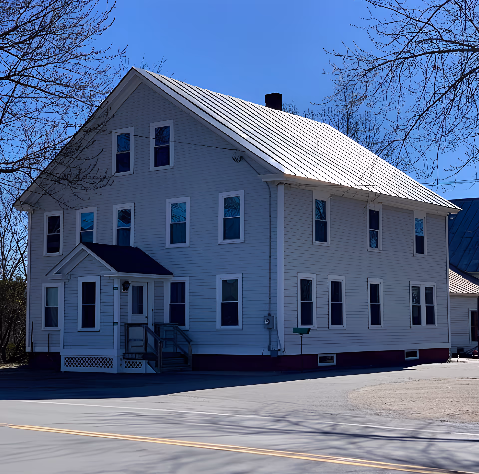 White multi-story house with many windows and a metal roof beside a road on a clear day.