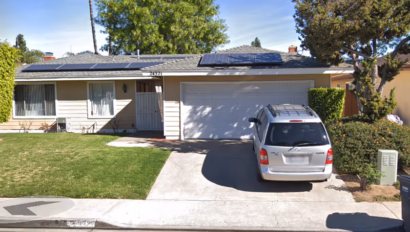 Front exterior of a single-story house with solar panels, a garage, driveway with a parked silver minivan, and a green lawn.