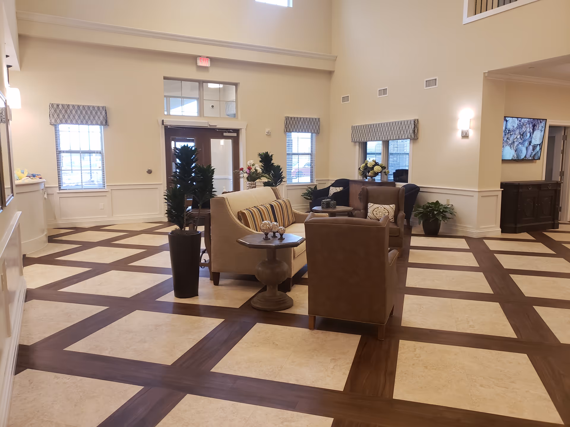 Light-filled lobby lounge with beige seating, plants, and checkered floor pattern.