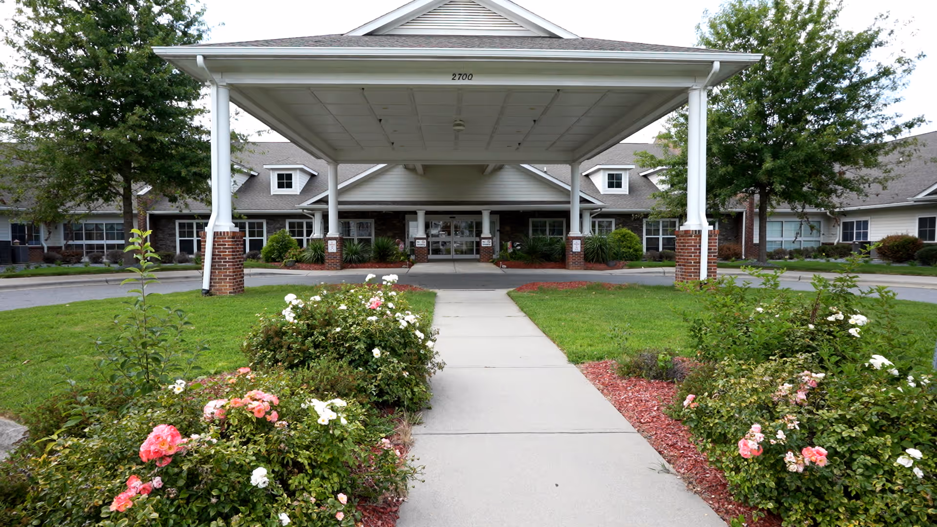 Front entrance of a senior living facility with a white canopy and landscaped walkway