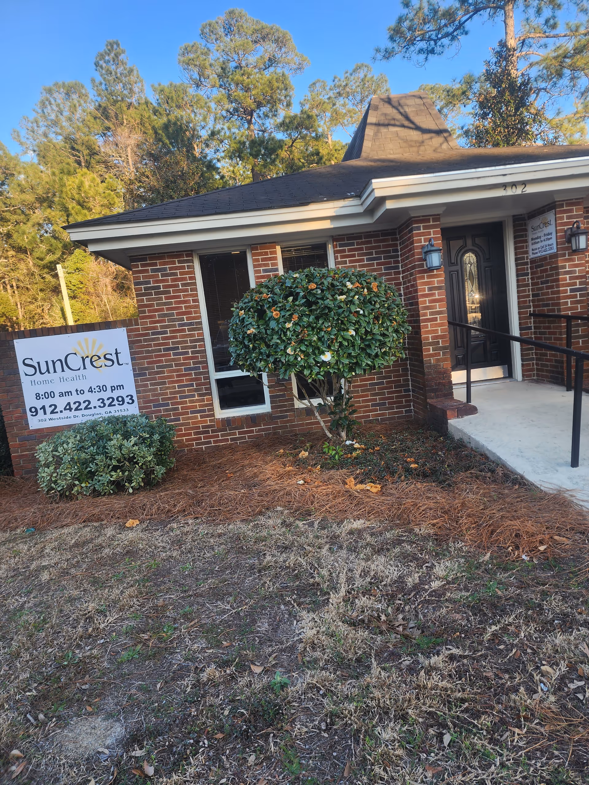 Brick SunCrest Home Health exterior with entrance, sign, steps, and landscaped shrubs.
