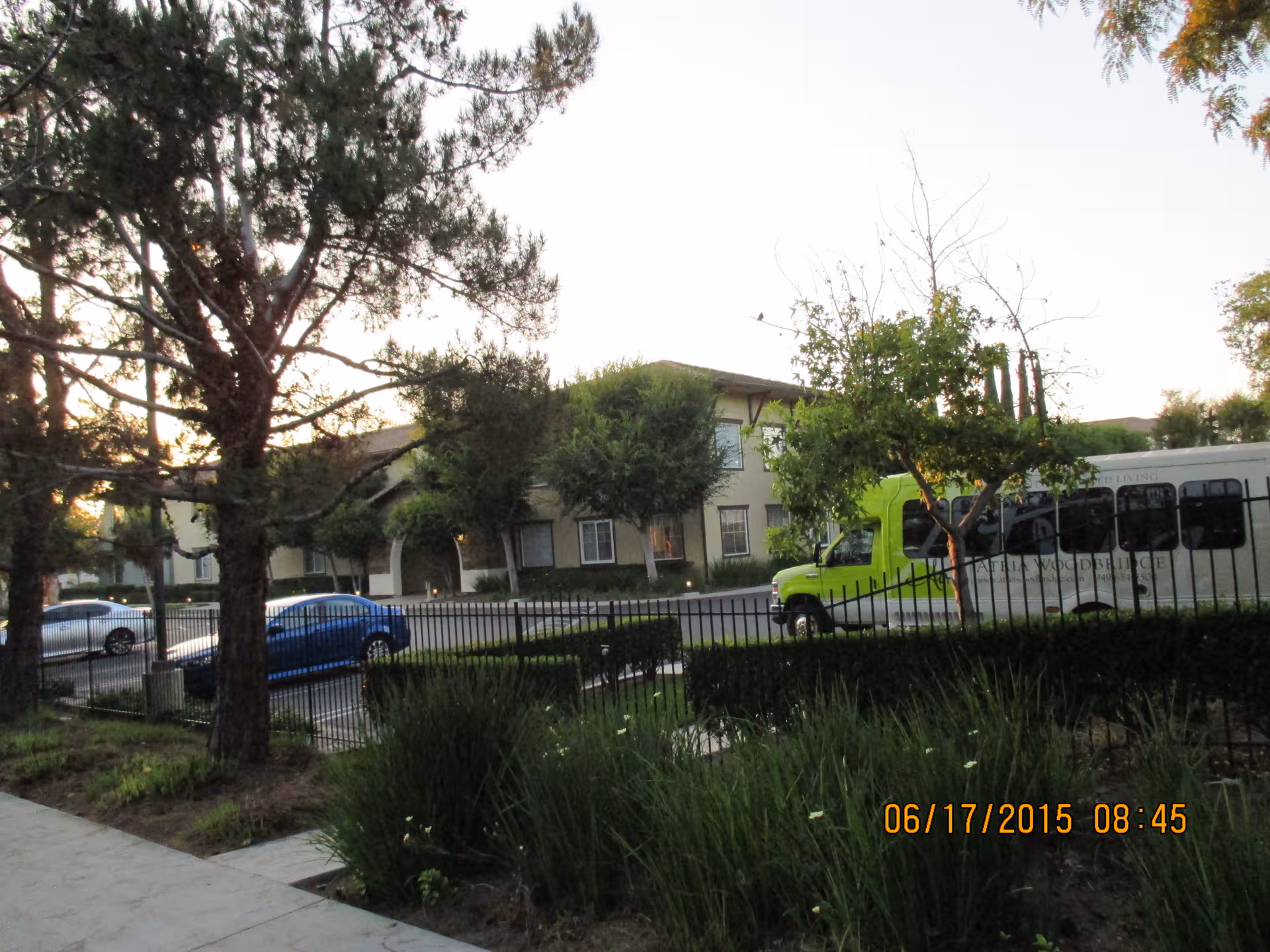 Exterior view of Woodbridge Terrace with a lime-green bus and parked cars along a landscaped front.