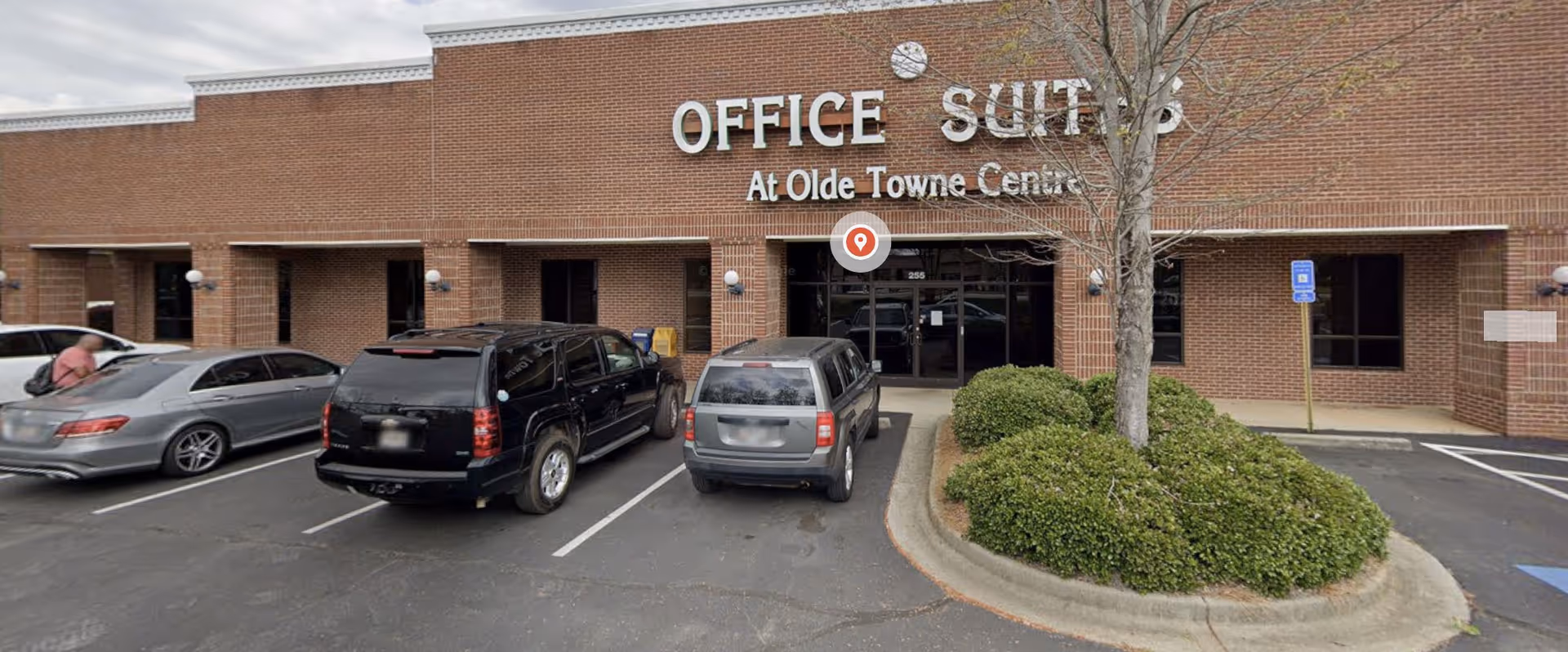 Brick storefront with large 'Office Suites' sign and several parked cars in front.