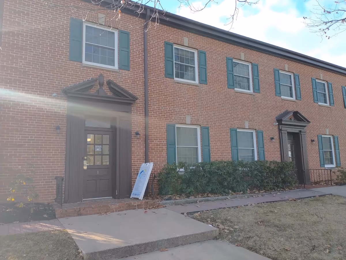 Brick senior living facility exterior with green shutters and two entry doors.