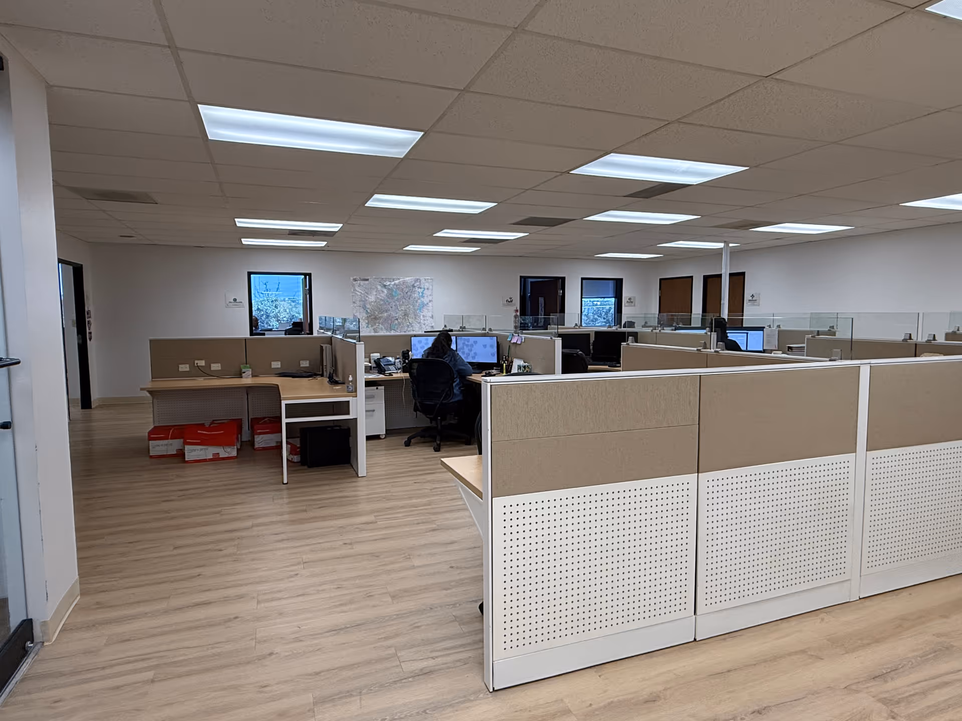 Open office cubicles with computers and a wall map in a bright facility workspace.