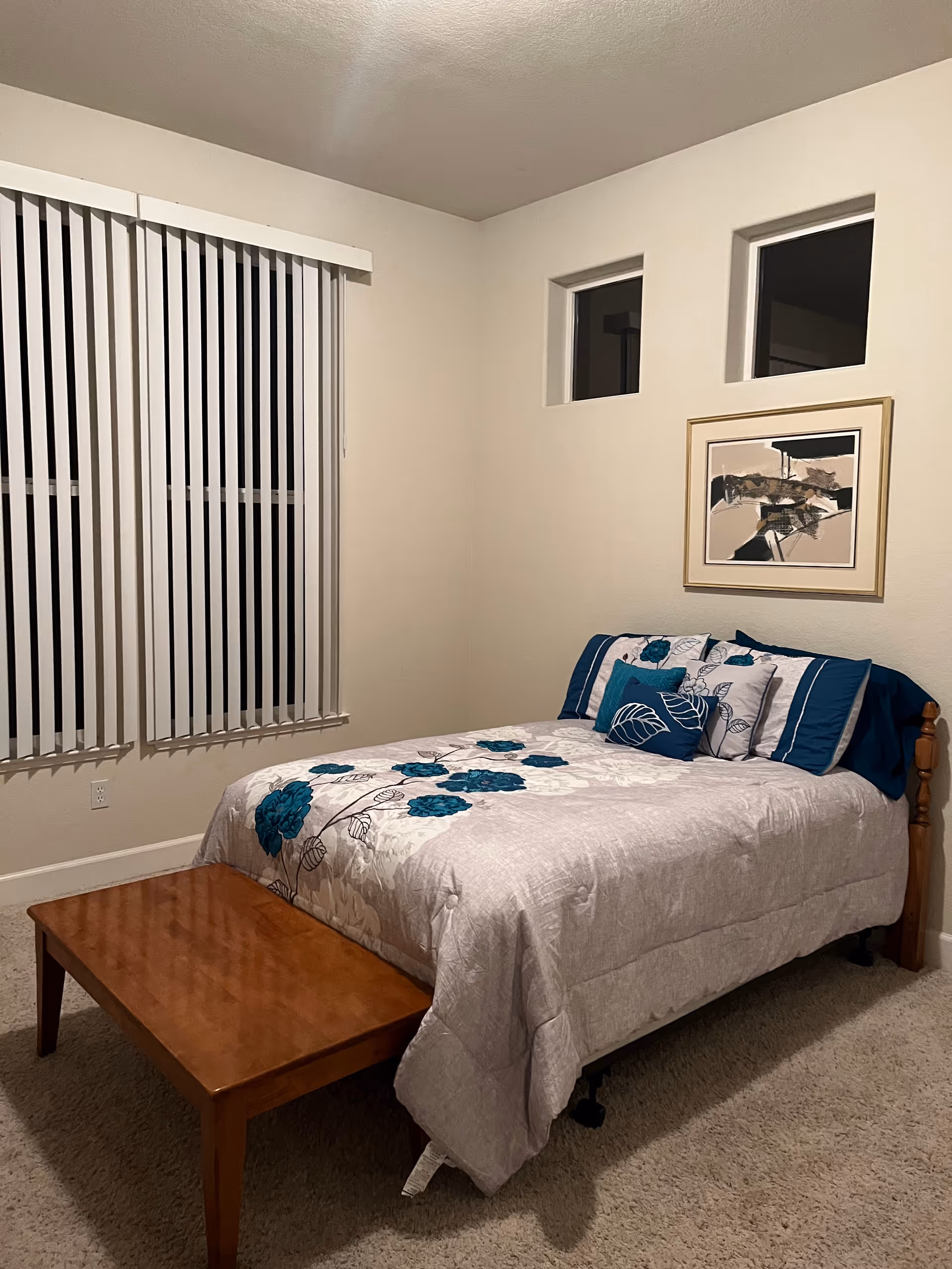Small bedroom with a neatly made bed featuring blue floral bedding and a wooden bench.