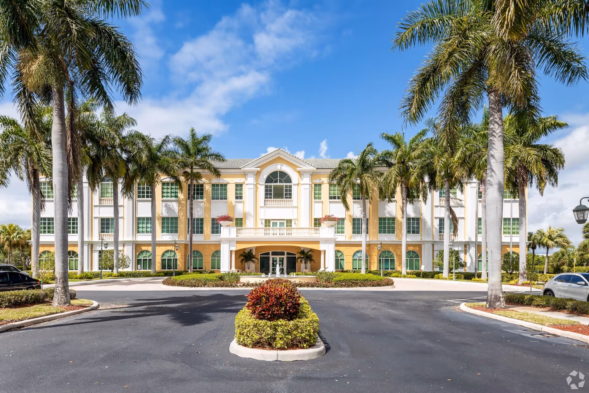 Front view of a large, palm-lined senior living facility with a circular driveway and entrance.