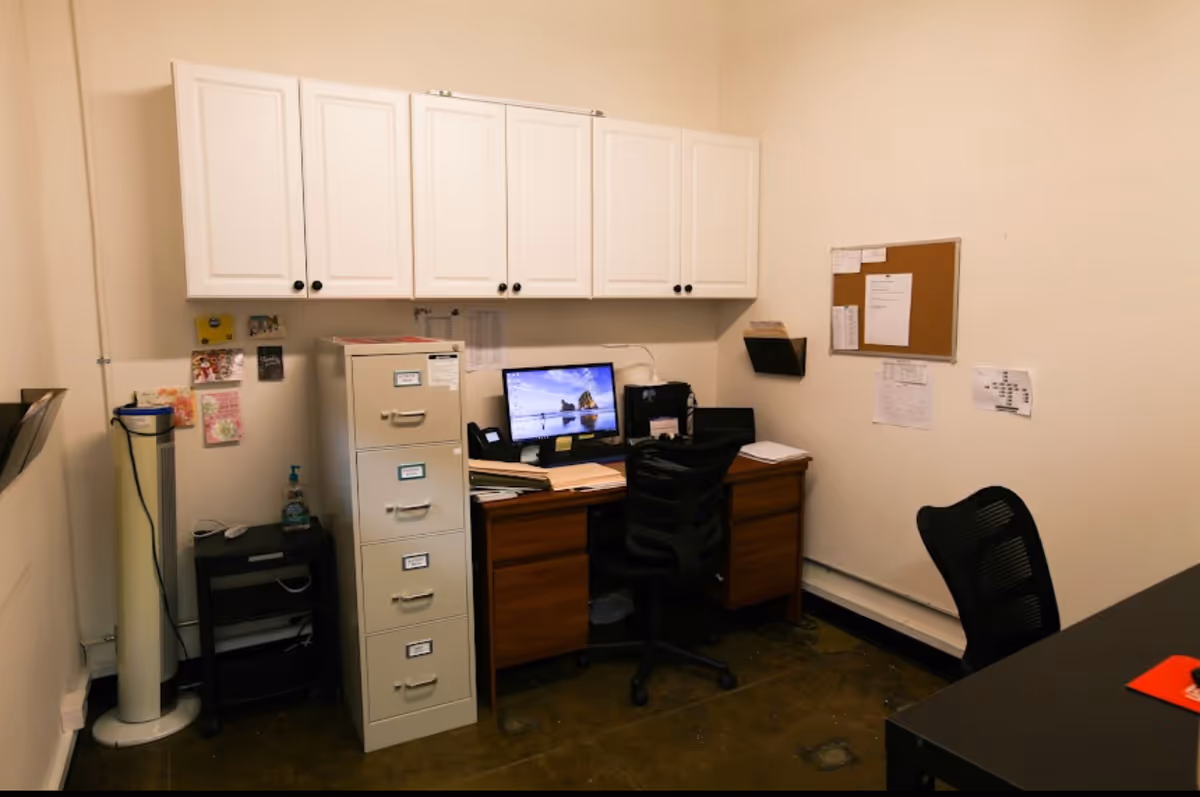 Office workspace with computer, filing cabinet, and white cabinets in a senior facility.