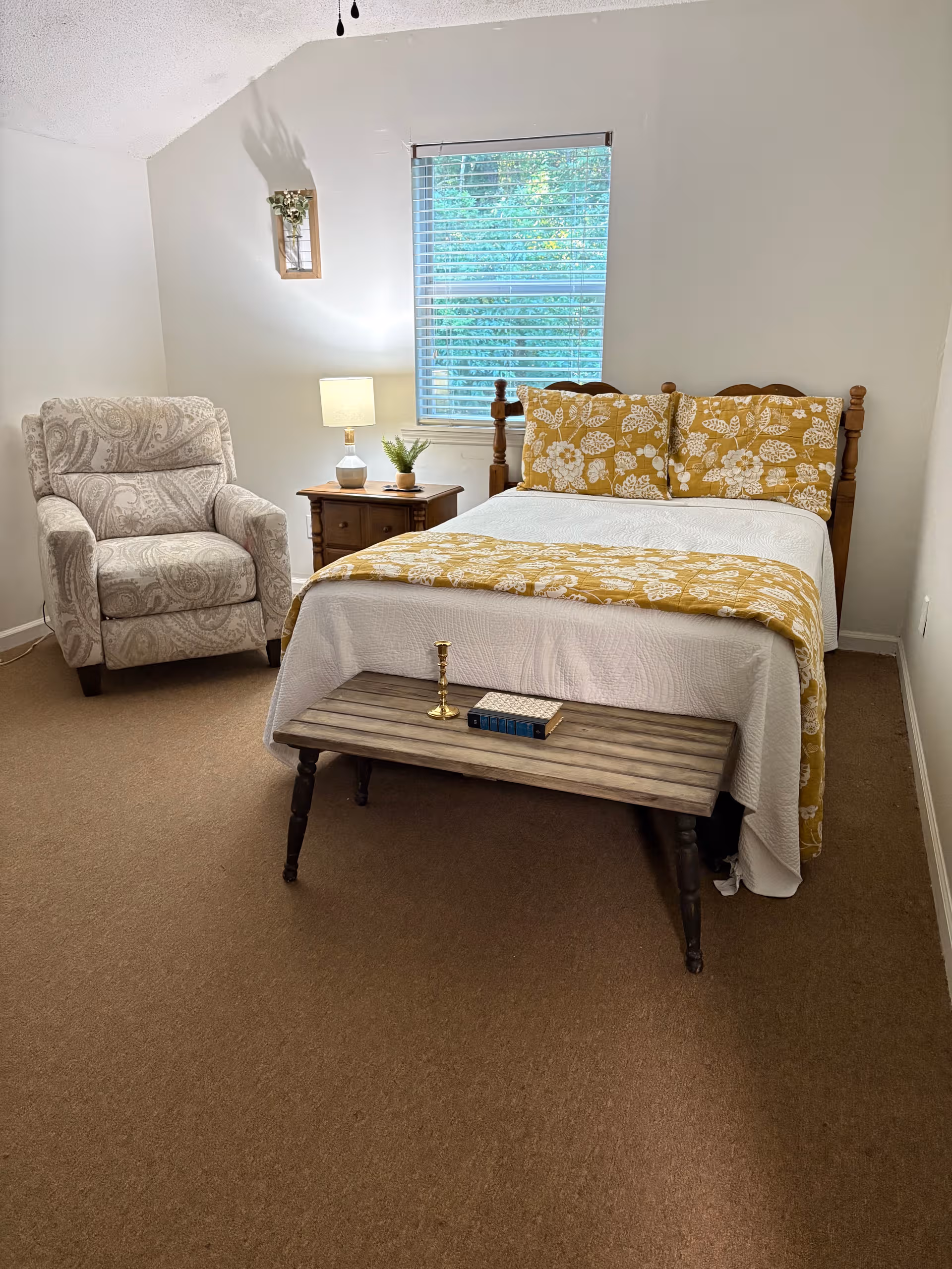 A cozy bedroom in a senior living facility with bed, chair, and nightstand.