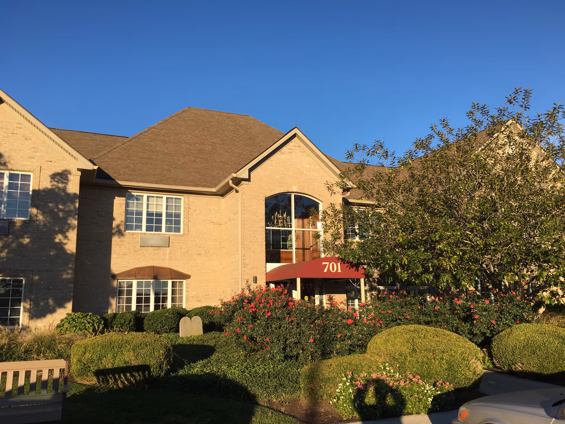 Brick senior living building with red canopy over entrance and landscaped shrubs.